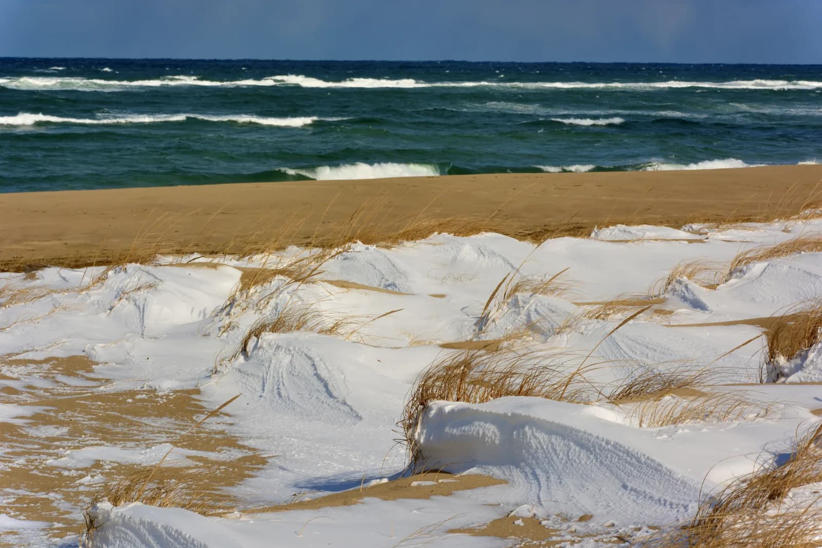Winter beach on Cape Cod with snow-covered dunes and ocean waves